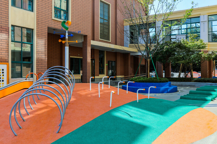 Playground with colorful, wavy rubber flooring in orange, green, and blue. Metal climbing arches and a weather vane add a playful atmosphere.